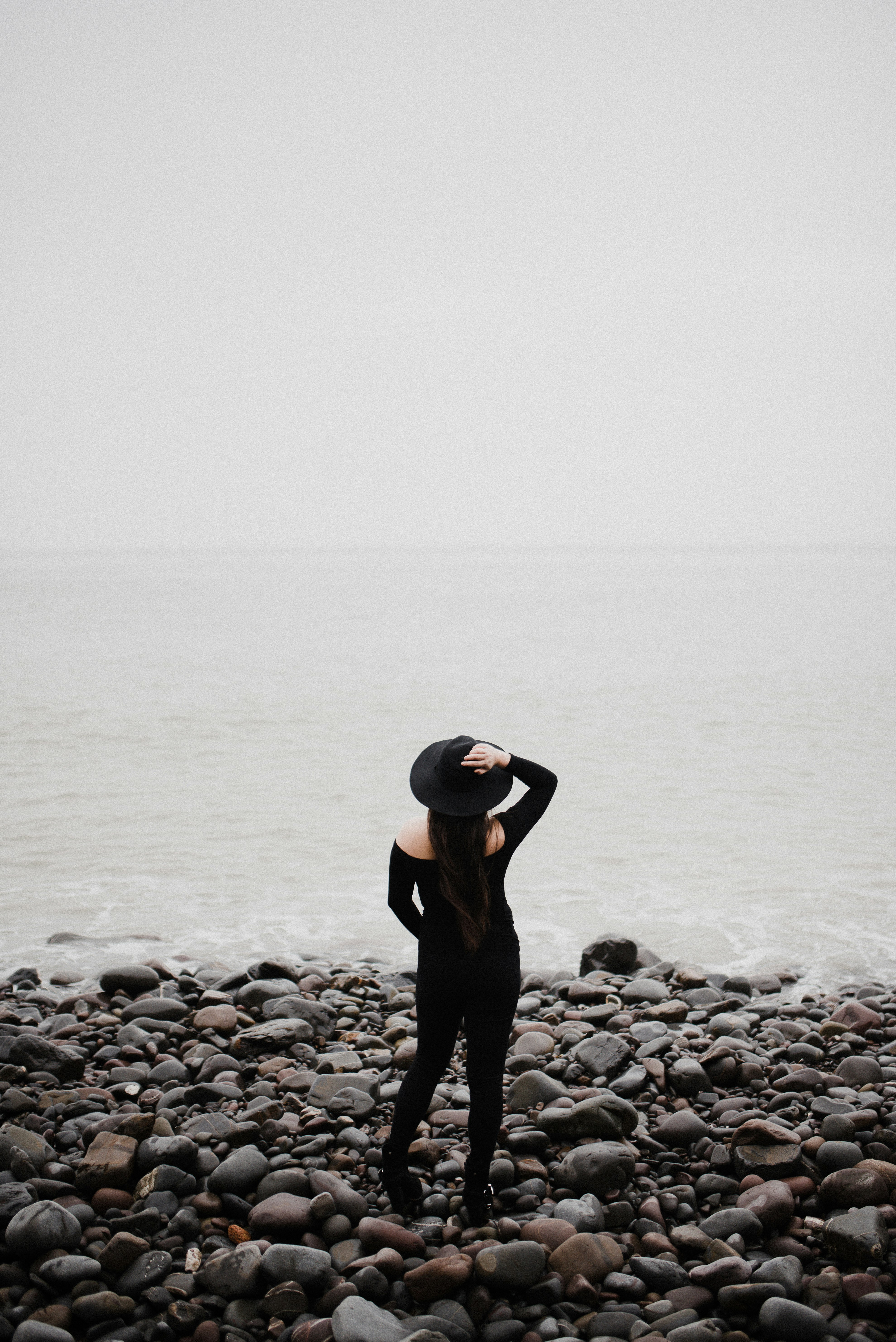 woman in black long sleeve shirt and black pants standing on rocky shore during daytime
